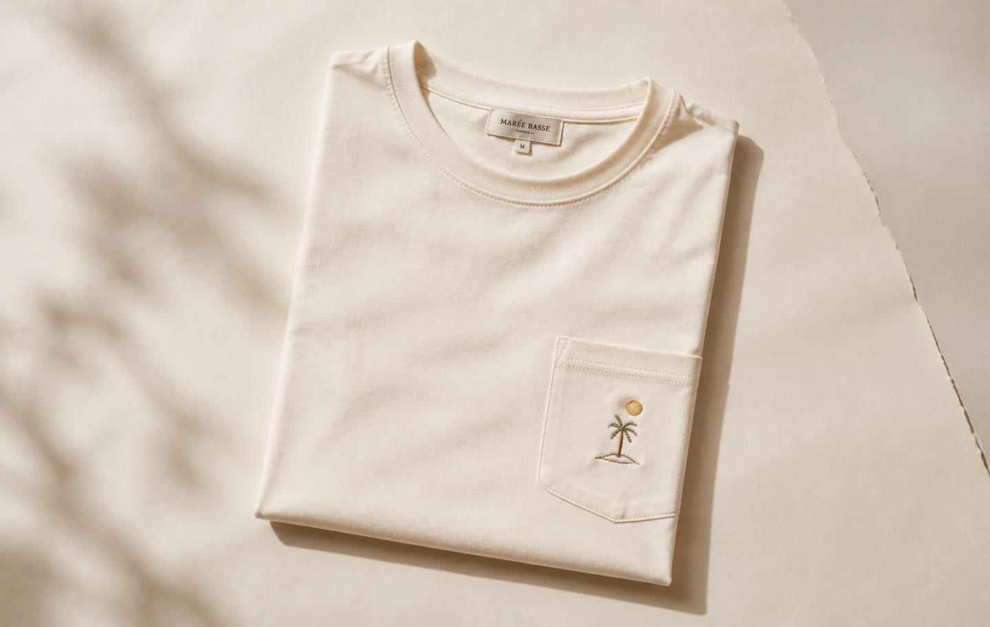 A folded cream pocket t-shirt on a neutral paper background